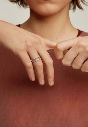 Anillos de plata en dos dedos, uno con pequeñas cuentas y el otro con una línea recta de piedras. La piel es clara y sin adornos.