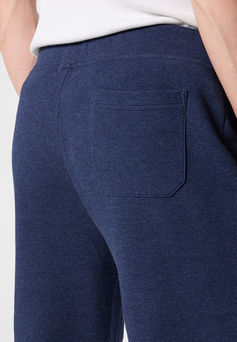 Granatowe, miękkie spodnie z tylną kieszenią. Materiał ma delikatny wzór splotu. Prosty krój, elastyczny pas.