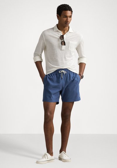Men's light gray long-sleeve polo with chest pocket, paired with blue swim shorts featuring an elastic waistband and white drawstring. White sneakers.
