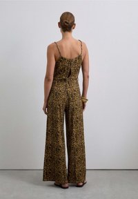 Mono de patrón floral con tirantes finos, piernas anchas, cintura ceñida y detalle de ojo de cerradura en la parte posterior; los colores incluyen amarillo oscuro y negro.