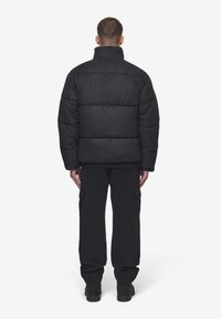 Giacca a vento nera con colletto alto, design trapuntato e finitura testurizzata. Indossata con pantaloni cargo neri abbinati e stivali.