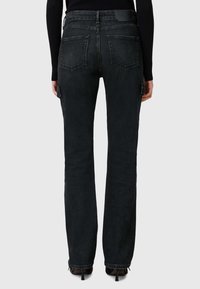 Jeans de mezclilla negra con un diseño de pierna recta, cinco bolsillos y una etiqueta de cuero en la parte trasera de la cintura. Tejido texturizado con costuras visibles.