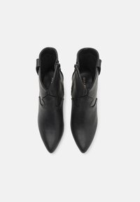 Bottes cheville en cuir noir avec bouts pointus, texture lisse, fermetures éclair latérales et couture détaillée sur le dessus.