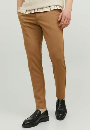Pantaloni khaki slim-fit realizzati in tessuto morbido, con tasche laterali, una texture liscia e dettagli di cucitura a contrasto. Scarpe nere completano il look.