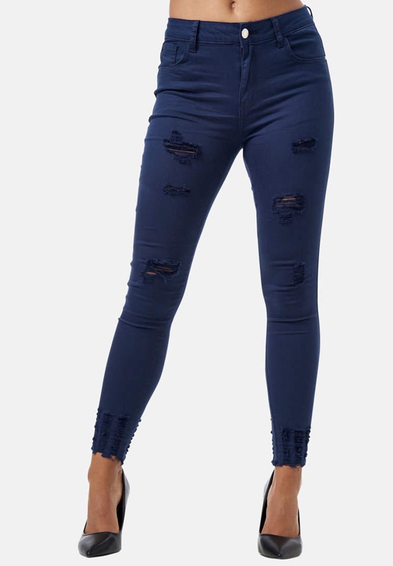 Jeans ajustados de color azul oscuro, hechos de denim, con parches rasgados y dobladillos deshilachados. Combinados con tacones altos negros.