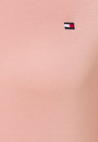 Pfirsichfarbendes, tailliertes T-Shirt aus gerippter Stoffqualität, mit einem kleinen gestickten Logo in Navy, Rot und Weiß auf der Brust.