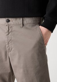 Světlé šedé chinos kalhoty vyrobené z měkké látky, s plochým předním dílem, bočními kapsami a knoflíkovým zapínáním v pase.
