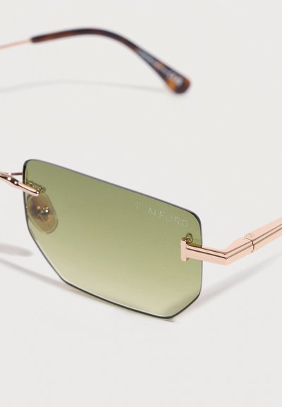 Γυαλιά ηλίου χωρίς σκελετό με φακούς με πράσινη απόχρωση και ροζ χρυσούς γεωμετρικούς βραχίονες, με χαραγμένο όνομα μάρκας στον φακό.