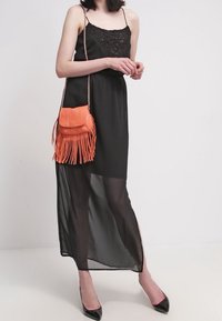 Černé maxi šaty bez rukávů s průhledným přehozem a krajkovými detaily. Kombinace soranžové tašky s třásněmi a řetízkem a černými podpatky.