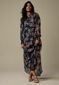 Long, flowy dress in dark navy with a floral pattern in pink and white. Made from lightweight fabric with a high-low hem and buttoned neckline.