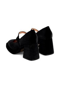 Scarpe con tacco alto in suede nero, con punta arrotondata, tacco a blocco spesso e dettagli con cinturino alla caviglia. Texture liscia e design semplice.