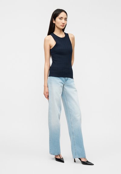 Μπλε σκούρο ριμπ αμάνικο τοπ με ψηλό λαιμό, συνδυασμένο με ανοιχτό γαλάζιο ψηλόμεσο τζιν και μαύρες μυτερές γόβες. Λείο ύφασμα, εφαρμοστή γραμμή.