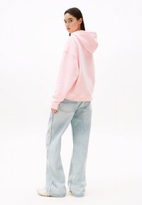 Sweatshirt à capuche rose surdimensionné avec des poignets côtelés, associé à un jean large bleu clair avec des bords effilochés et des détails de couture subtils.