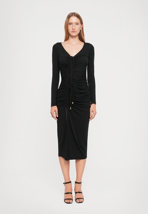 Black long-sleeve dress with ruching, V-neckline, front slit, and gold-button detail at the waist. Smooth fabric with a fitted silhouette.