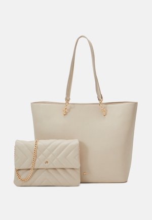 Twee beige handtassen, een grote tote met dubbele handvatten en een doorgestikte crossbody met een gouden kettingband, getoond tegen een effen achtergrond.