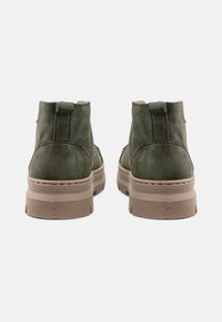 Stivaletti alla caviglia verde in suede con punta rotonda, suola beige testurizzata e piccolo passante sul retro. Presentano dettagli cuciti lungo la suola.