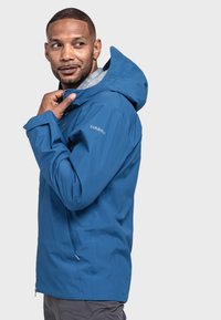 Blauer wasserfester Jacke mit Kapuze, ausgestattet mit einem Reißverschluss vorne und einem weichen Innenfutter. Logo auf dem linken Ärmel, elegantes Design.