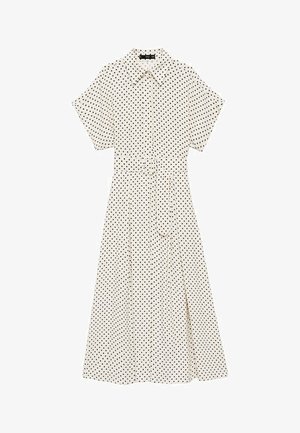 Ecru jurk met zwarte stippen. Korte mouwen, kraag, riem in de taille en een vloeiende rok. Lichtgewicht stof.
