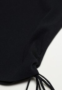 Vêtement en tricot noir avec une surface texturée, présentant un détail froncé à l'ourlet et des cordons de serrage réglables sur un côté.