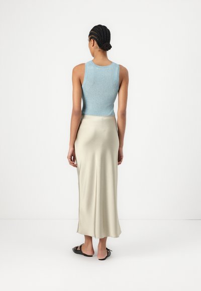 Haut sans manches côtelé bleu clair associé à une longue jupe lisse ivoire. Le mannequin porte des chaussures noires à enfiler ; design minimaliste.