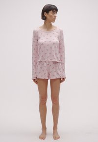 Σετ πιτζάμες ανοιχτό ροζ με μακρυμάνικη μπλούζα και σορτς, με μικρά μοτίβα φιόγκων. Απαλό ύφασμα, χαλαρή εφαρμογή, μίνιμαλ σχεδιασμός.