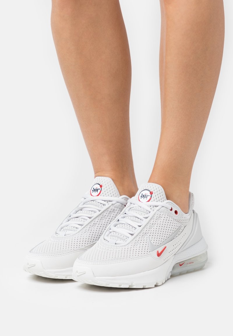 Baskets Nike Air Max en mesh blanc avec petits logos rouges portées sur des jambes nues sur un fond blanc uni.