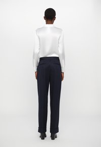 White satin long-sleeve blouse paired with navy pinstriped trousers. Trousers have rolled cuffs and a tailored fit. Smooth texture throughout.