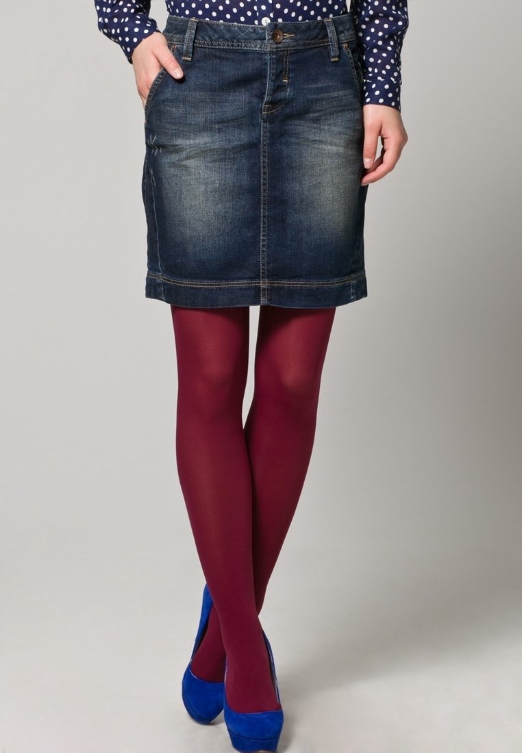 La falda de mezclilla tiene una longitud hasta medio muslo, color azul oscuro y un ligero desgaste. Se combina con medias burdeos y tacones altos azules.