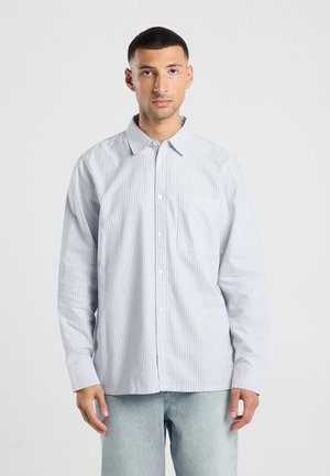 Lichtblauw gestreept overhemd met lange mouwen, een button-down kraag, een voorzak en een subtiele textuur; gecombineerd met lichte spijkerbroeken.