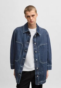 Donkerblauwe denimjack met een kraag, voorkeurszakken en knoopsluitingen. Heeft een ontspannen pasvorm en zichtbare stikseldetails.