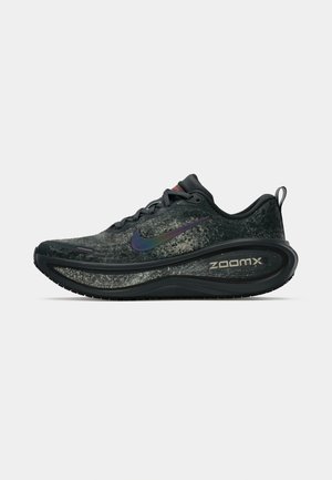 Zwarte en grijze Nike ZoomX hardloopschoen met iriserend swoosh-logo, dikke gevoerde zool, veters en een trekhaak op een effen witte achtergrond.