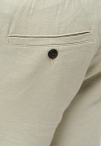 Μπεζ ύφασμα με πίσω τσέπη που διαθέτει κλείσιμο με κουμπί σε ένα ζευγάρι παντελόνια.