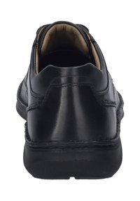 Chaussure en cuir noir avec une texture lisse, arrière arrondi et doublure intérieure contrastante en tan. Présente des coutures discrètes et une semelle en caoutchouc résistante.