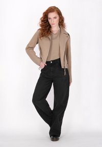 Chaqueta de moto de cuero beige con cremalleras, combinada con pantalones vaqueros negros anchos, sobre un fondo blanco liso.