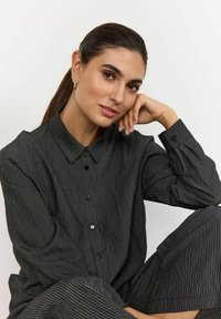 Black striped button-up shirt with long sleeves, featuring a collar and relaxed fit. Smooth fabric, with subtle vertical lines and black buttons.