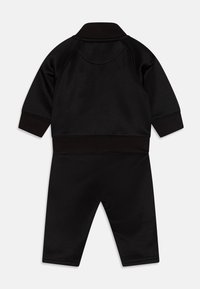 Completo sportivo nero a due pezzi, composto da una giacca con zip e colletto e pantaloni abbinati, entrambi realizzati in un tessuto liscio e elastico.