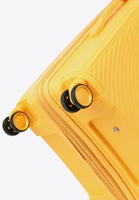 Valigia rigida gialla con motivo a righe, texture liscia, doppie ruote con accenti neri e chiusura a cerniera.
