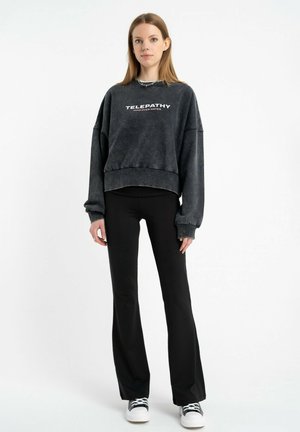 Czarny, krótki sweatshirt z nadrukiem "TELEPATHY", z szerokimi rękawami i miękką fakturą, w połączeniu z dopasowanymi czarnymi spodniami i białymi sneakersami.