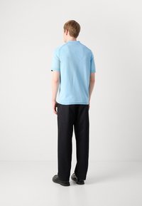 Polo shirt azul claro com mangas curtas, colarinho canelado e tecido texturizado, combinado com calças largas pretas e sapatos pretos.