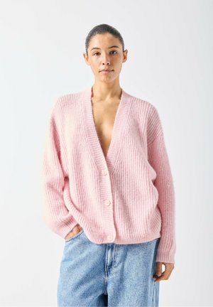 Rosa gerippte Strickjacke mit tiefem V-Ausschnitt, sechs Knöpfen und lockerer Passform, kombiniert mit hellblauen Jeans. Weiches, strukturiertes Material.