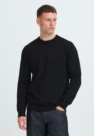 Black knitted sweater with a round neckline and long sleeves. Features ribbed cuffs and hem, worn with dark denim jeans. Simple design.