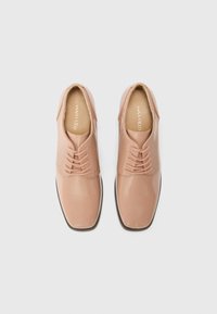 Light pink patent leather dress shoes with a smooth finish, featuring five eyelets, thin laces, and a rounded toe. Textured insole visible.