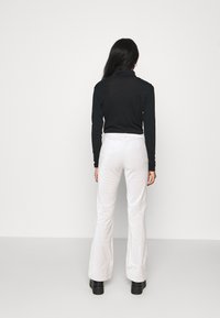 Un col roulé noir, style ajusté, associé à un pantalon blanc évasé, texture lisse, et des bottes noires massives contrastantes. Fond simple.