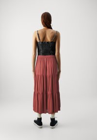 Haut smocké noir et jupe maxi en rust, avec des bretelles ajustables, un tissu fluide, le tout porté avec des baskets montantes noires.