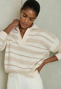 Beige stribet sweater med en afslappet pasform, krave og lange ærmer. Blød tekstur med skiftende lyse og mørke striber i varierende bredder.