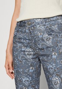 Blå mönstrade denimjeans har intrikata blommönster i ljusa och mörka nyanser, med funktionella fickor och en metallknappstängning.