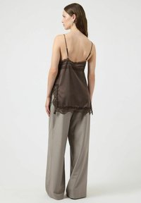 Brązowa satynowa koszulka na ramiączkach z koronkową lamówką, regulowanymi ramiączkami, warstwowym koronkowym dołem, w zestawie z luźnymi, jasnoszarymi spodniami.