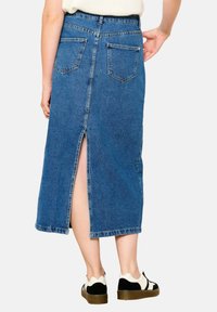 Mėlyna džinsinė midi sijonas su užpakaline skeltute, turintis kišenes ir prigludusią taliją. Medžiaga turi būdingą džinsinį tekstūrą.