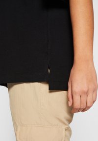 Černé tričko s krátkým rukávem a bočními rozparky, vyrobené z bavlny, spárované s béžovými cargo kalhotami s velkou kapsou. Hladká textura.