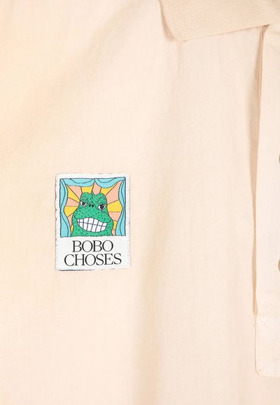 Patch carré sur tissu beige montrant une grenouille verte souriante avec des rayons de soleil derrière et le texte "BOBO CHOSES" en dessous.